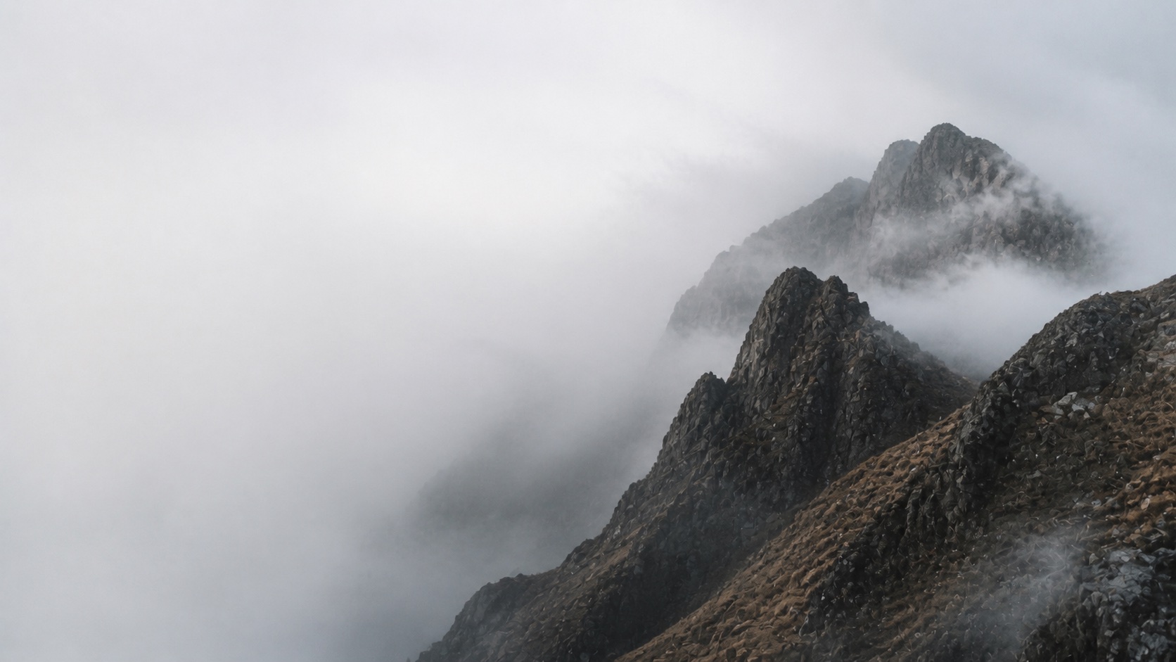 A dark mountain ridge emerging through pale clouds